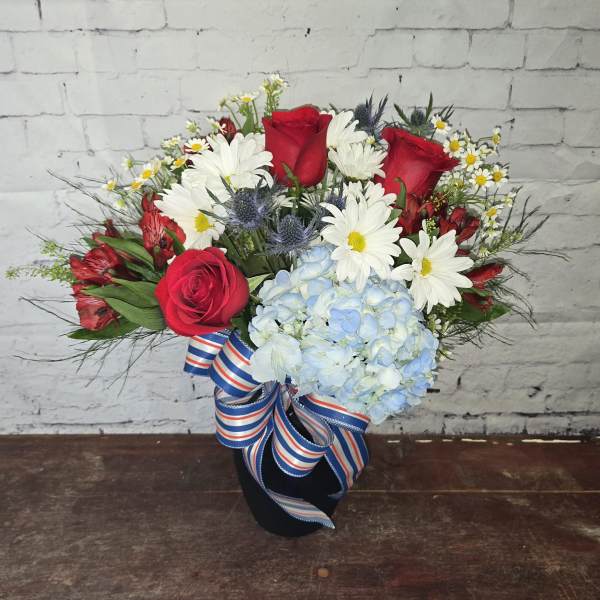 Bouquet of red roses, white daisies, and blue hydrangea in a black vase