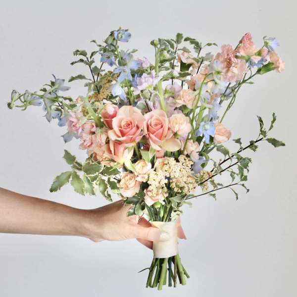 Handheld bouquet of peach roses and blue flowers