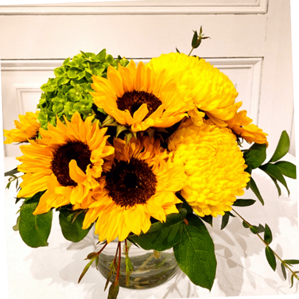 Yellow sunflowers and mums arranged in a clear glass vase