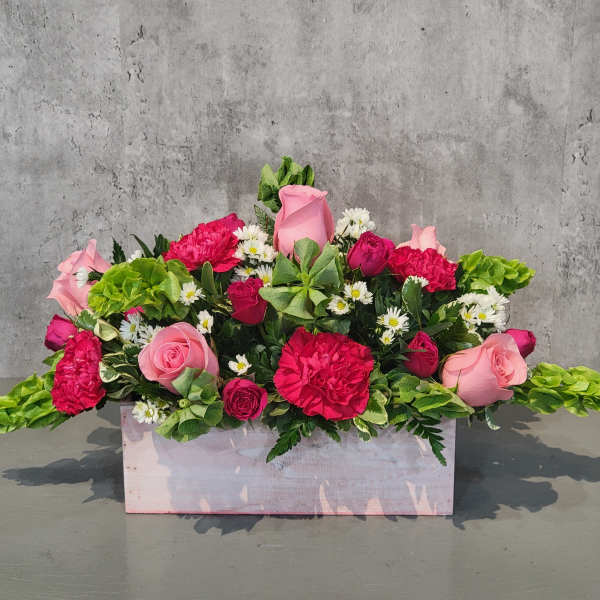 Pink and red flower arrangement in a pale wooden box
