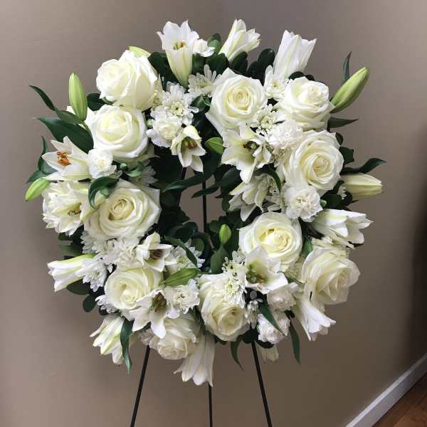 White floral wreath on a black stand with roses and lilies