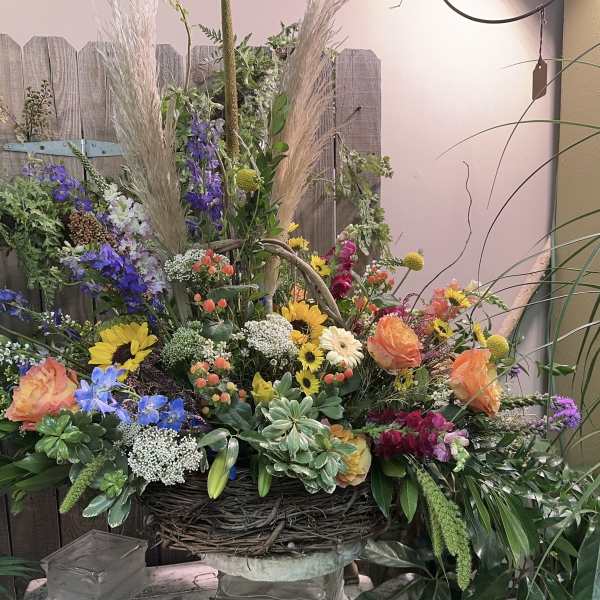 Large mixed floral arrangement in a woven basket with tall grasses and bright blooms