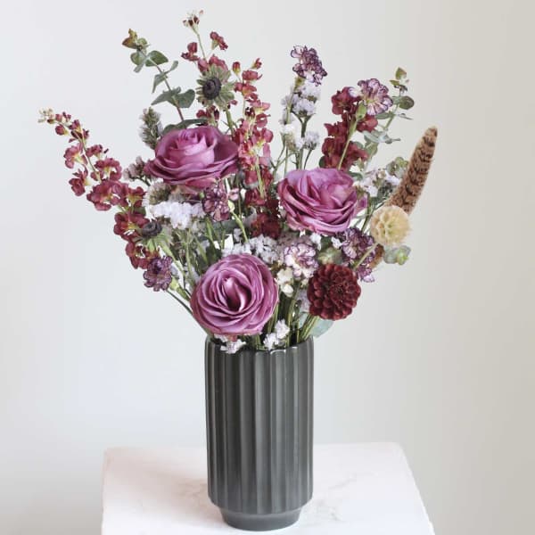 Purple floral arrangement in a ribbed dark vase