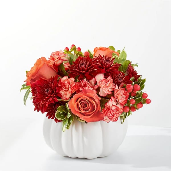 Orange and red floral arrangement in a white pumpkin vase