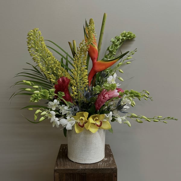 Tropical flower arrangement in a white vase with orchids and heliconia