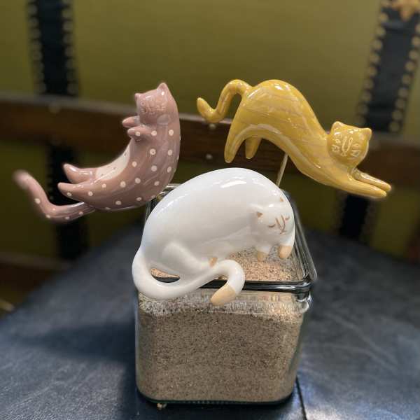 Three ceramic cat figurines rest on a glass container filled with sand.