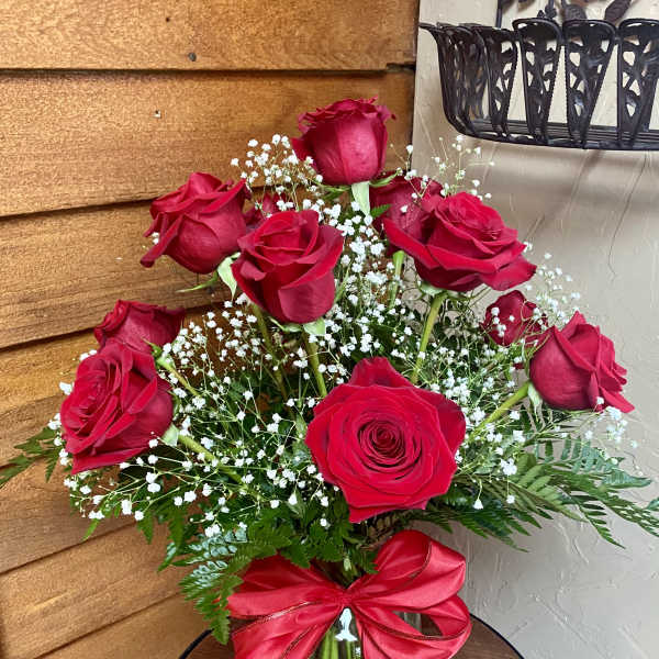 Red roses arranged in a glass vase with baby's breath and a red ribbon.