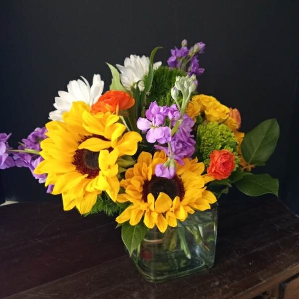 Mixed bouquet with sunflowers, daisies, and purple flowers in a glass vase