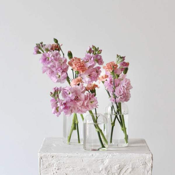 Pink and peach flowers in three clear glass vases on a white pedestal.