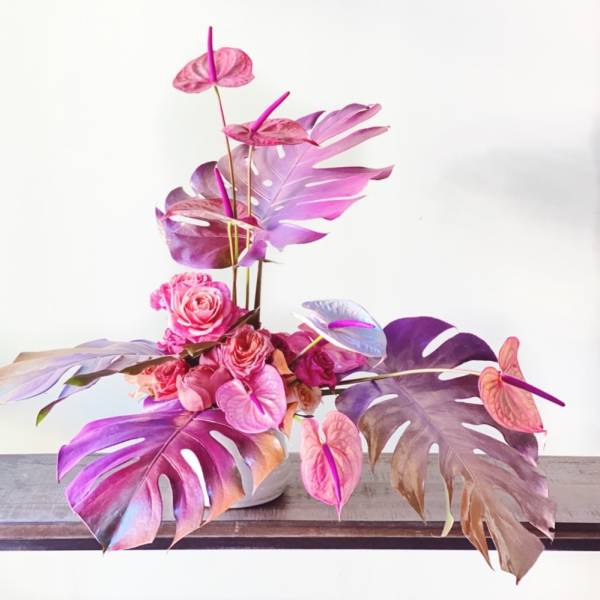 Pink and purple floral arrangement with monstera leaves in a white vase