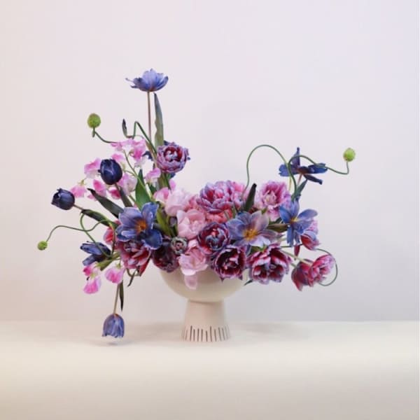 Colorful bouquet of pink and blue flowers in a white pedestal vase