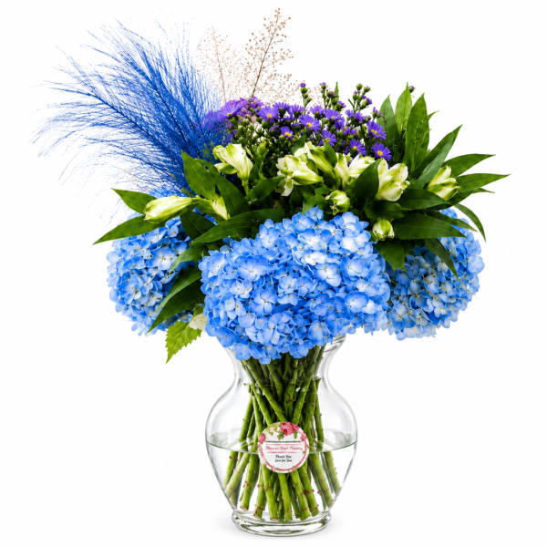 Blue hydrangeas and purple daisies in a clear glass vase