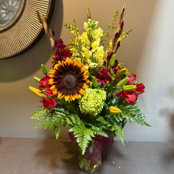 Mixed bouquet with a sunflower, red blooms, and yellow snapdragons in a glass vase