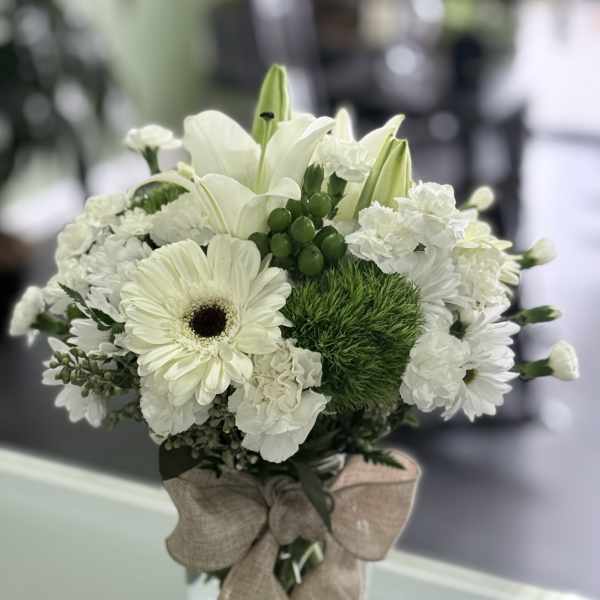 White floral bouquet in a clear glass vase with a burlap bow