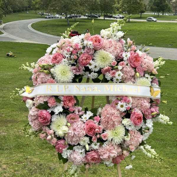 Pink and white funeral wreath on an easel with a memorial ribbon