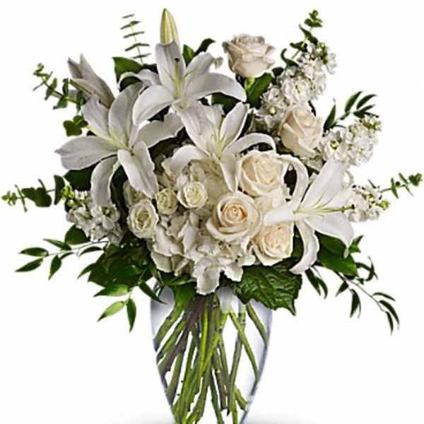 White lilies, roses, and hydrangeas arranged in a clear glass vase