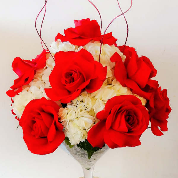 Red roses and white hydrangeas in a wine glass vase with curly red accents