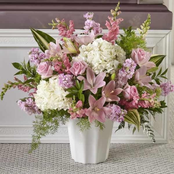 Pink lilies and roses arranged with white hydrangeas in a white vase.