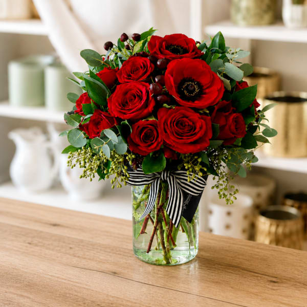 Red roses and anemones in a glass vase with a striped ribbon