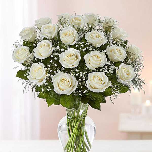 Arrangement of white roses with filler flowers in a clear glass vase