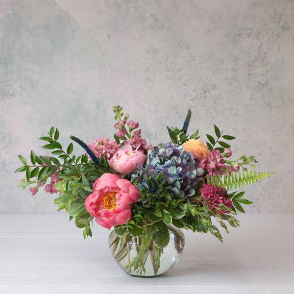 Mixed bouquet of pink and blue flowers in a clear glass vase