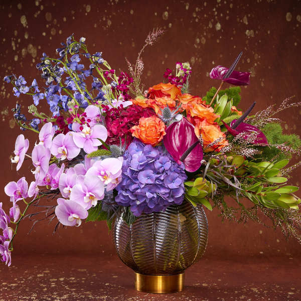 Colorful mixed bouquet in a round glass vase with orchids and hydrangeas