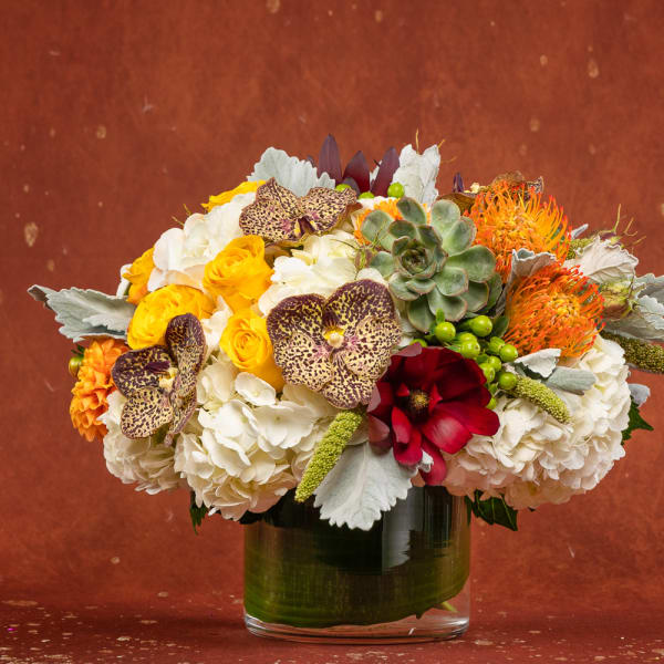 Mixed bouquet in a glass vase with white hydrangeas, yellow roses, and orange accents