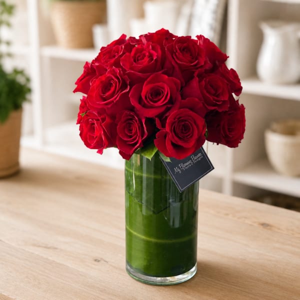Red roses arranged in a tall glass vase on a table
