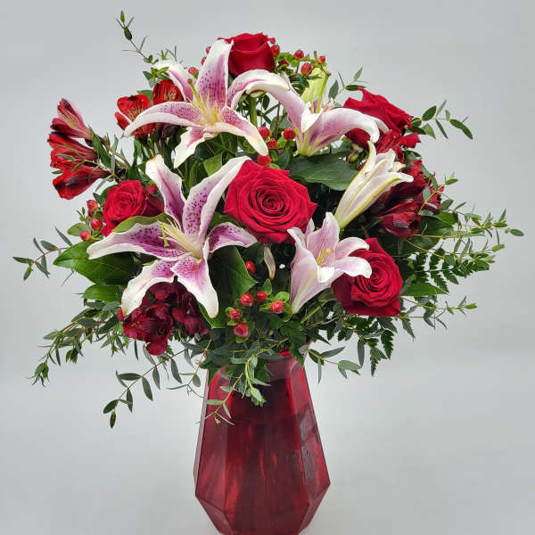 Bouquet of red roses and pink lilies in a red glass vase