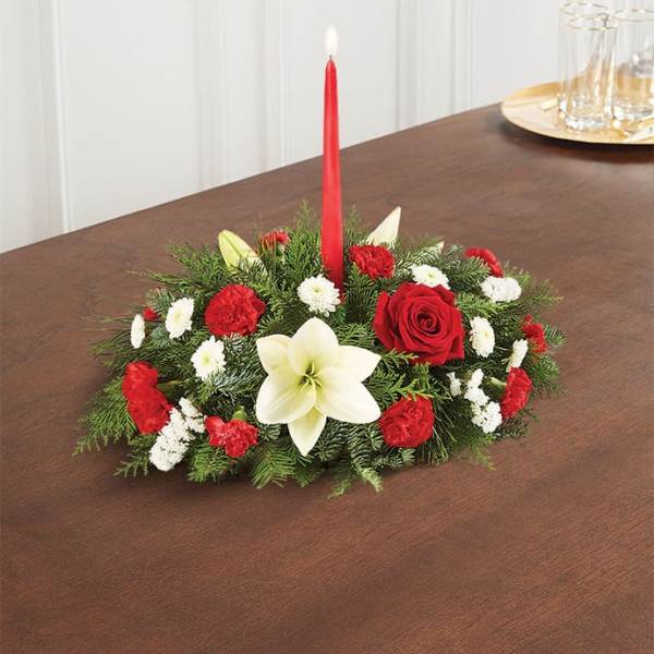 Low holiday centerpiece with red and white flowers and a red taper candle