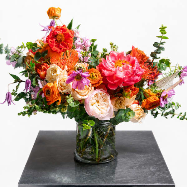 Mixed bouquet of orange, pink, and purple flowers in a glass vase