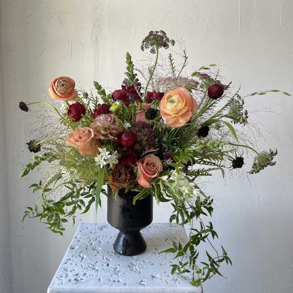 Mixed bouquet of peach and burgundy flowers in a black vase