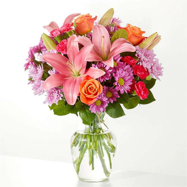 Bouquet of pink lilies, roses, and purple daisies in a clear glass vase