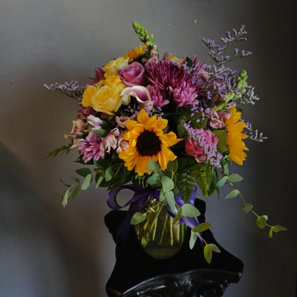 Mixed bouquet with sunflowers, roses, and purple flowers in a glass vase