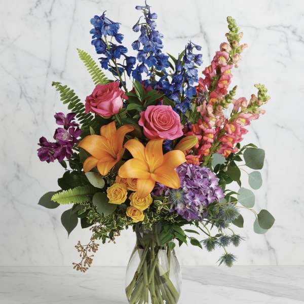 Colorful bouquet with roses, lilies, delphinium, and snapdragons in a glass vase