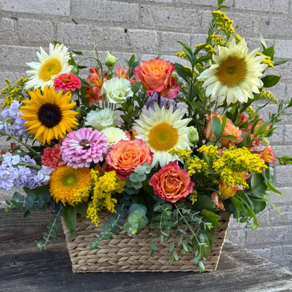 Mixed bouquet in a woven basket with sunflowers, roses, and pastel blooms