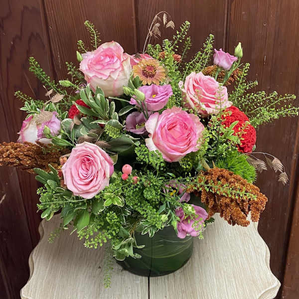 Mixed arrangement of pink roses and purple blooms in a leaf-wrapped glass vase