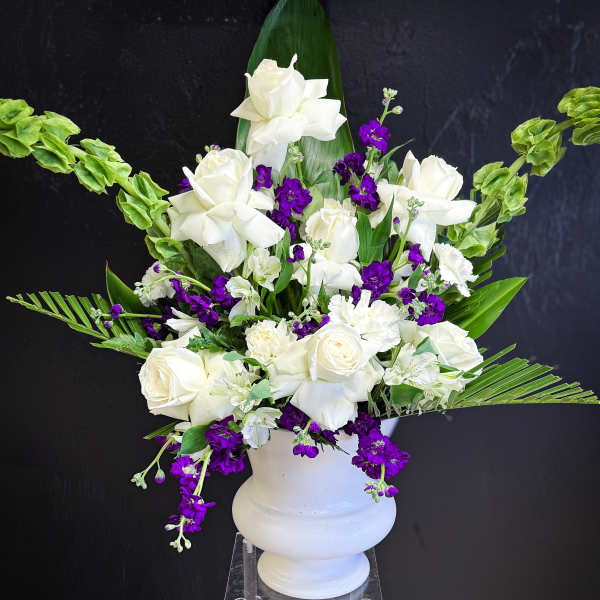 White roses and purple flowers arranged in a white urn vase