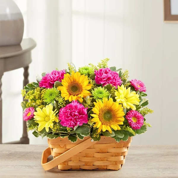 Basket of yellow sunflowers, pink carnations, and daisies