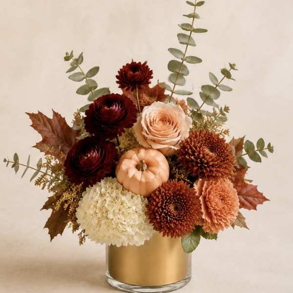 Autumn floral arrangement in a gold vase with a small pumpkin centerpiece