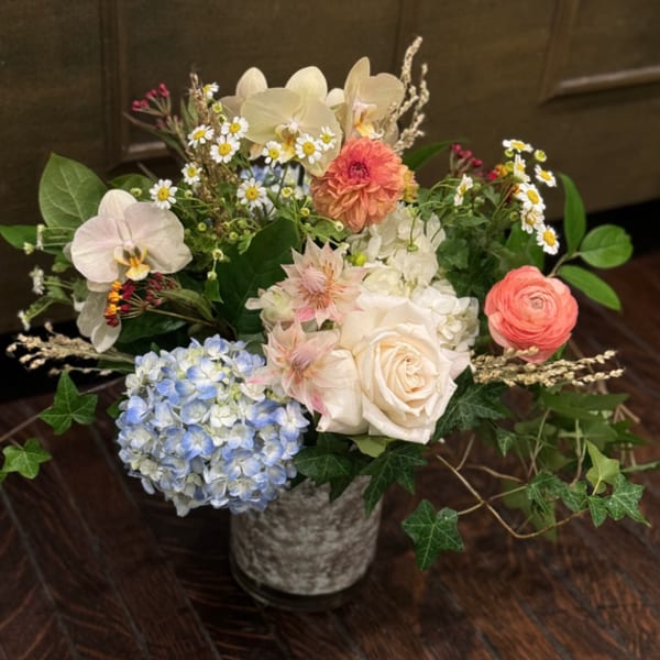 Mixed bouquet in a gray vase with orchids, roses, hydrangea, and small daisies