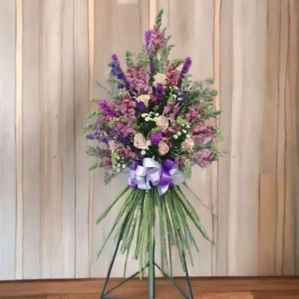 Tall standing floral spray with purple and pink flowers and a ribbon bow
