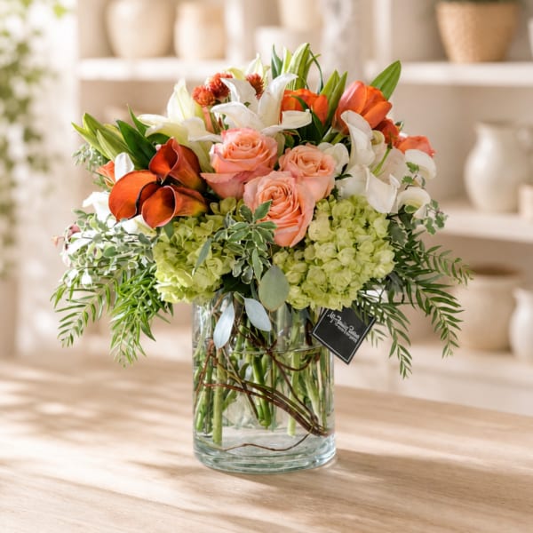 Mixed bouquet of roses, lilies, and orange blooms in a glass vase