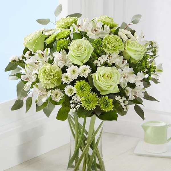 Green and white bouquet of roses, carnations, and daisies in a clear glass vase
