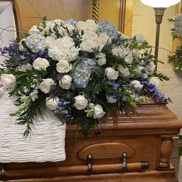 Large white and blue floral spray on a wooden casket