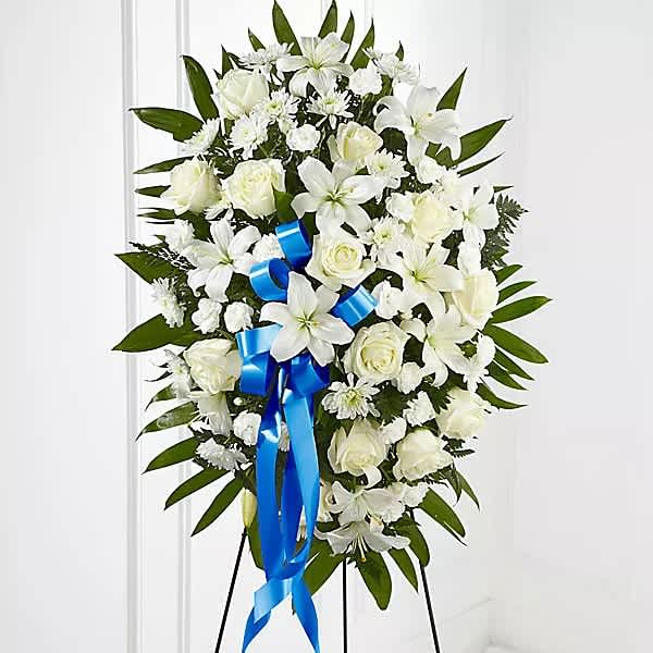 White funeral spray with lilies, roses, and a blue ribbon on an easel