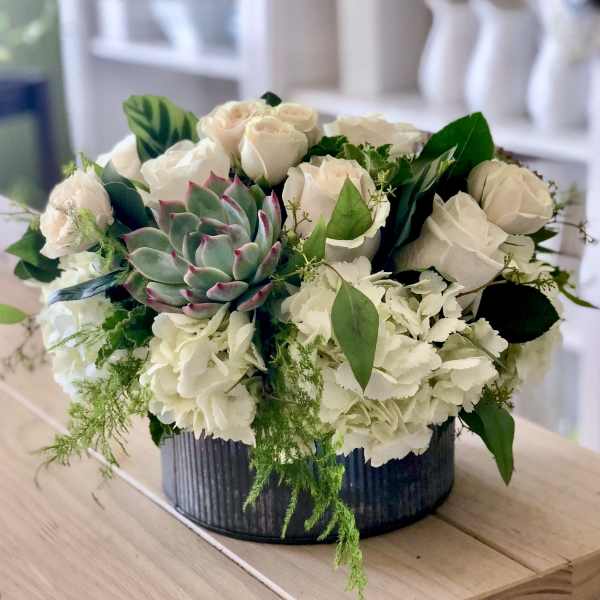 White roses and hydrangeas with a succulent in a dark round container