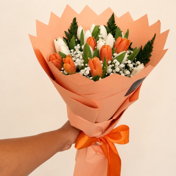Handheld bouquet of orange and white tulips wrapped in peach paper
