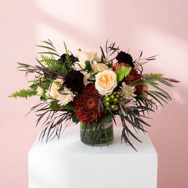 Mixed bouquet of cream, peach, and burgundy flowers in a glass vase