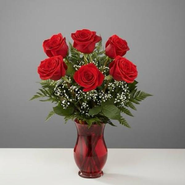 Red roses arranged in a red glass vase with baby's breath